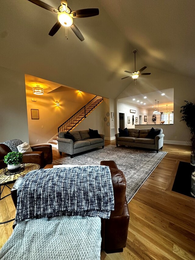 living room featuring baseboards, ceiling fan, stairway, wood finished floors, and vaulted ceiling