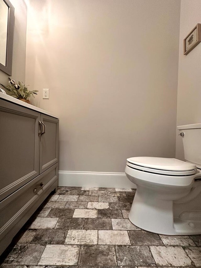 bathroom with toilet, stone finish flooring, baseboards, and vanity