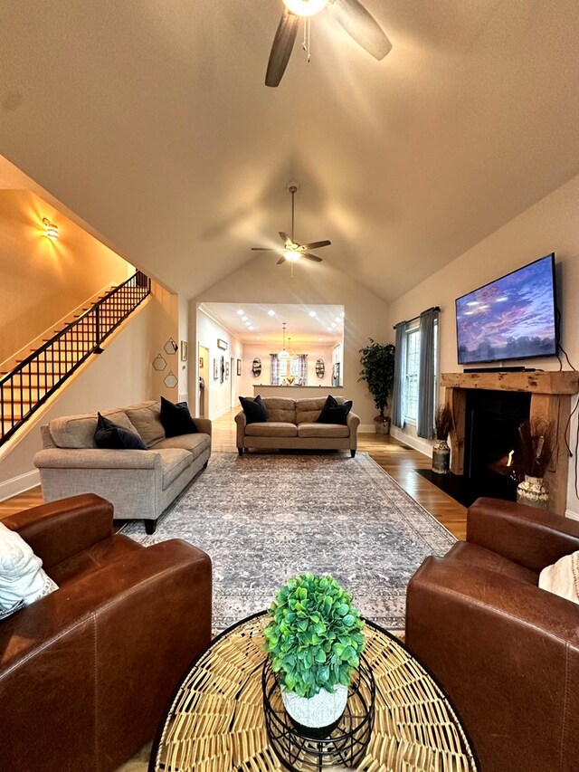 living room featuring ceiling fan, a fireplace with flush hearth, wood finished floors, stairs, and vaulted ceiling