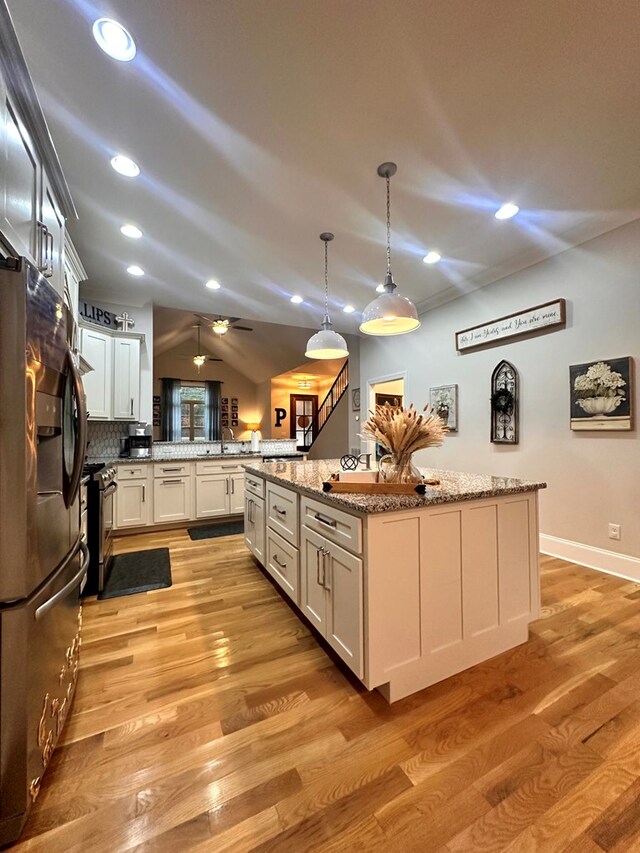 kitchen with a peninsula, stainless steel appliances, vaulted ceiling, a center island, and pendant lighting