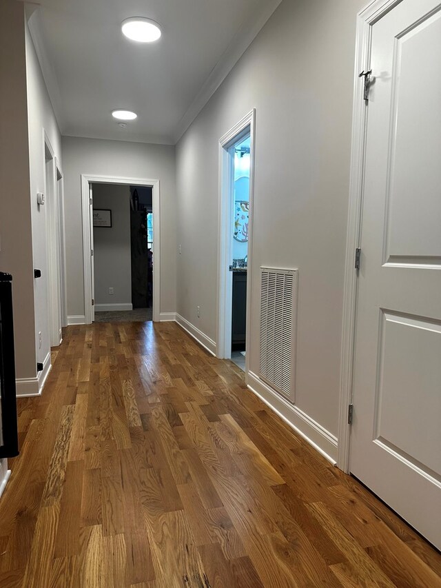 corridor featuring baseboards, visible vents, wood finished floors, and ornamental molding