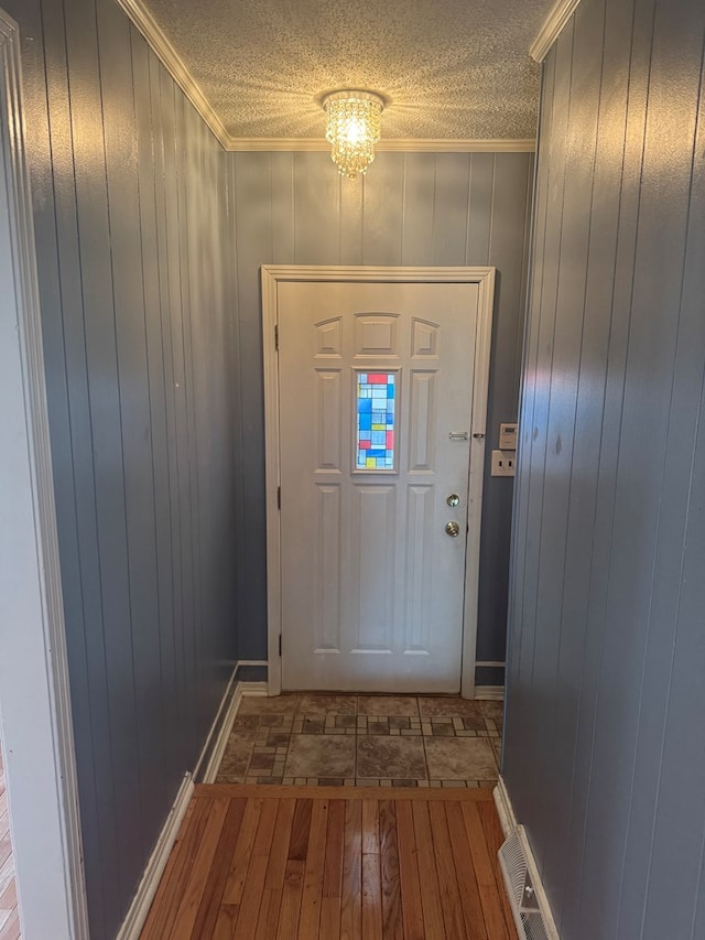 entryway with baseboards, visible vents, wood finished floors, crown molding, and a textured ceiling