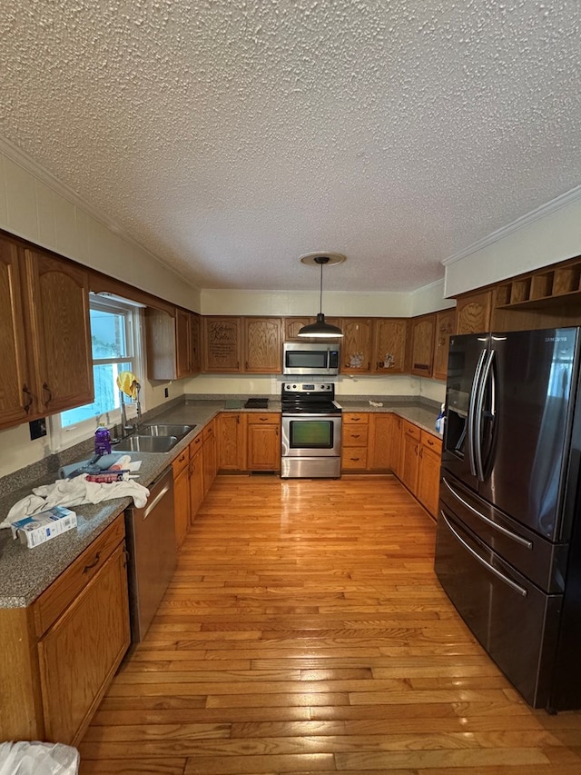 kitchen featuring a sink, appliances with stainless steel finishes, brown cabinetry, dark countertops, and pendant lighting