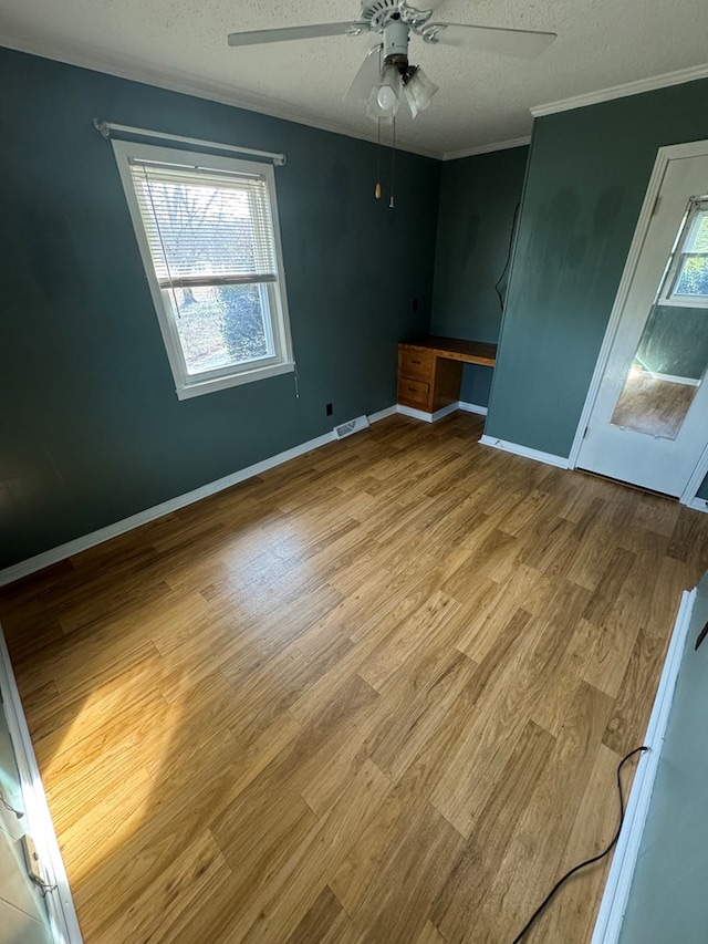 interior space with a textured ceiling, ornamental molding, built in desk, and light wood-style floors