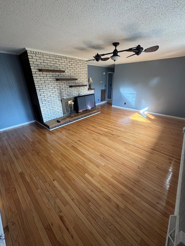 unfurnished living room with a textured ceiling, wood finished floors, a ceiling fan, baseboards, and a brick fireplace