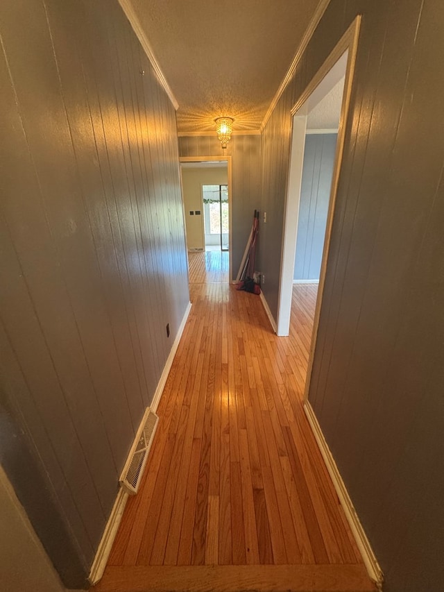 hallway featuring visible vents, light wood-style floors, ornamental molding, a textured ceiling, and baseboards