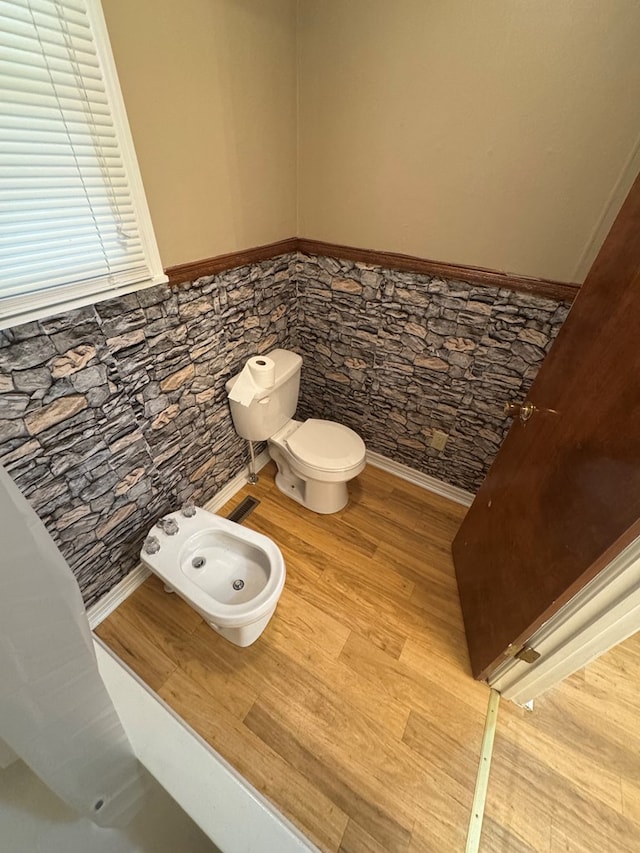 half bathroom featuring toilet, a wainscoted wall, a bidet, and wood finished floors