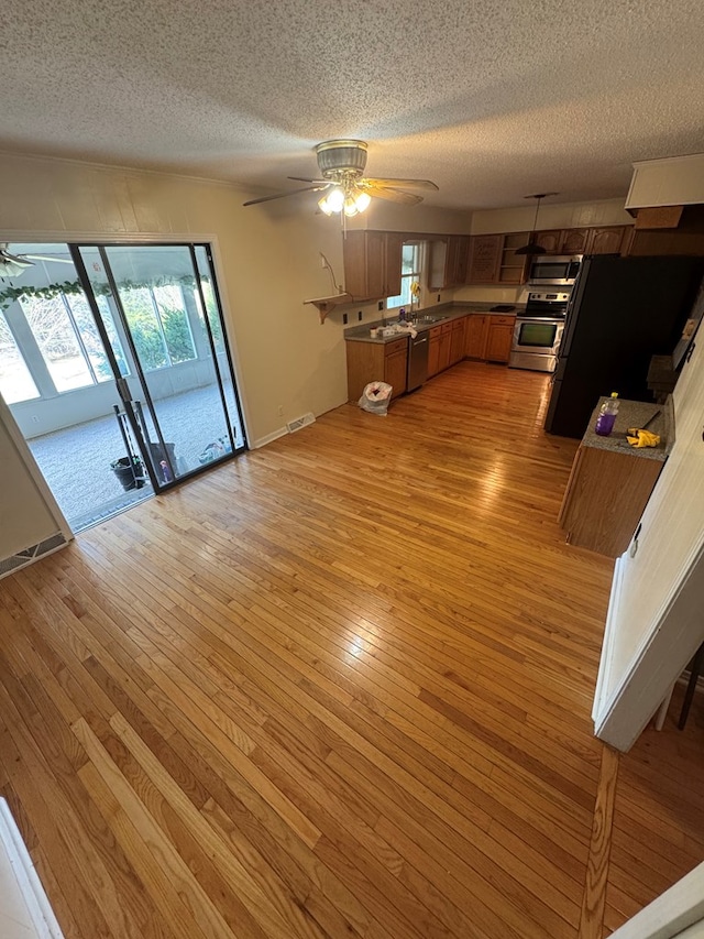 unfurnished living room with a ceiling fan, light wood-type flooring, visible vents, and a textured ceiling