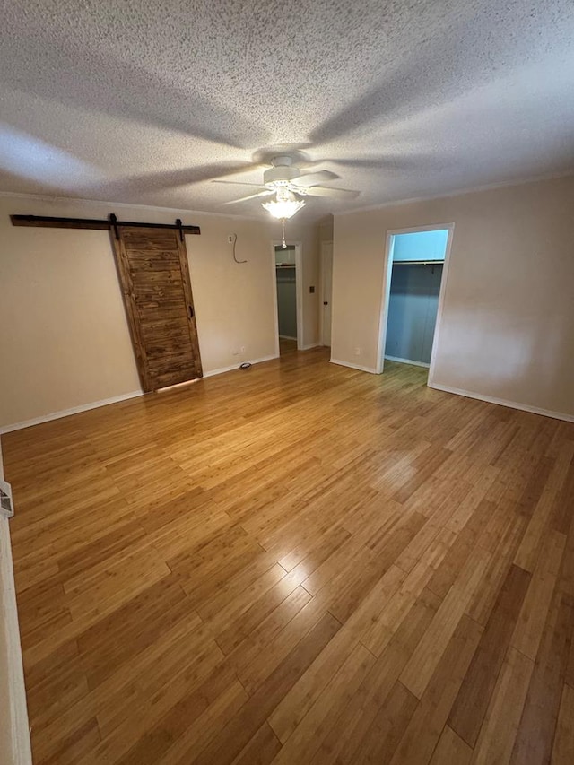 unfurnished room featuring a barn door, baseboards, a ceiling fan, a textured ceiling, and light wood-type flooring