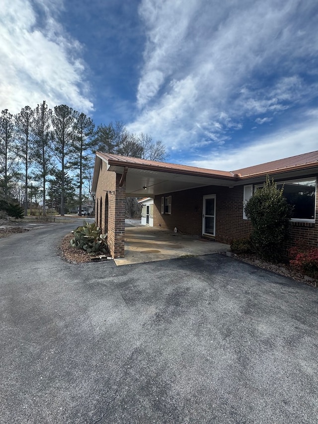 view of side of home with driveway, a carport, and brick siding