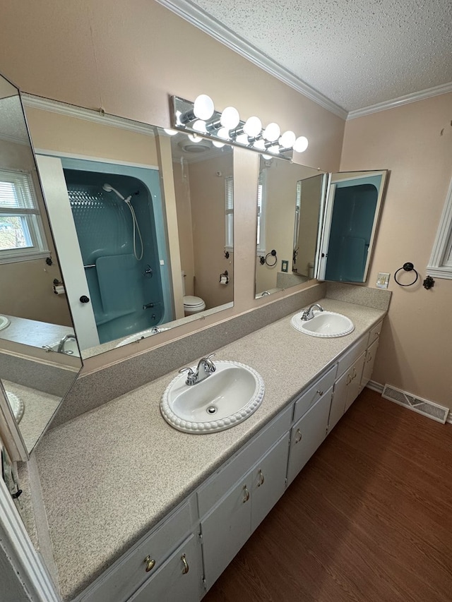 bathroom with wood finished floors, ornamental molding, a sink, and visible vents