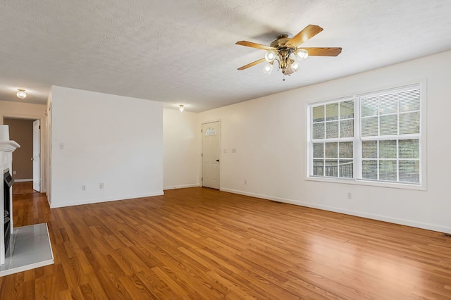 unfurnished living room with a textured ceiling, ceiling fan, wood finished floors, a fireplace with flush hearth, and baseboards