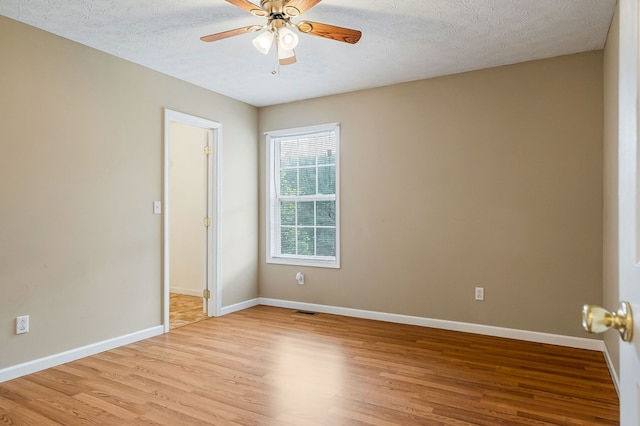 spare room featuring a textured ceiling, visible vents, a ceiling fan, baseboards, and light wood finished floors