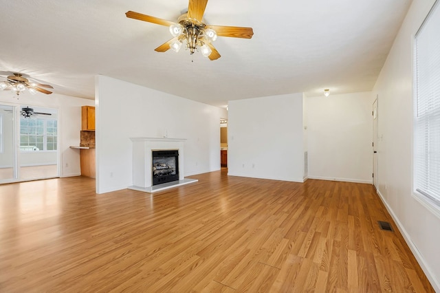 unfurnished living room featuring visible vents, a fireplace with raised hearth, baseboards, ceiling fan, and light wood-style floors