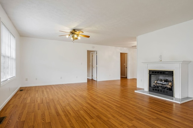 unfurnished living room featuring a ceiling fan, a fireplace with raised hearth, visible vents, and wood finished floors