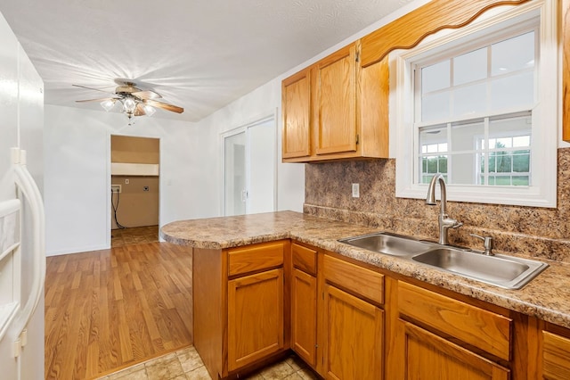 kitchen featuring tasteful backsplash, a peninsula, light countertops, white fridge with ice dispenser, and a sink