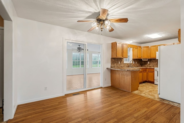 kitchen with light wood finished floors, tasteful backsplash, a sink, white appliances, and a peninsula