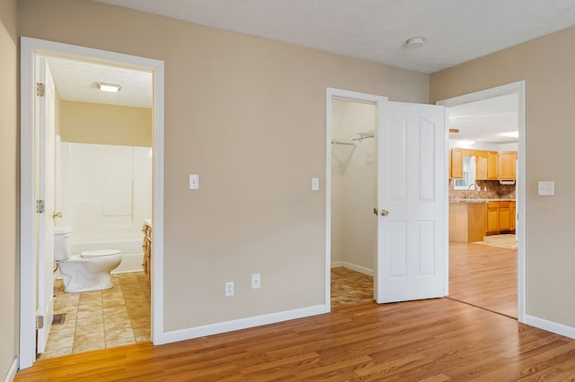 unfurnished bedroom featuring light wood finished floors, baseboards, connected bathroom, a spacious closet, and a closet