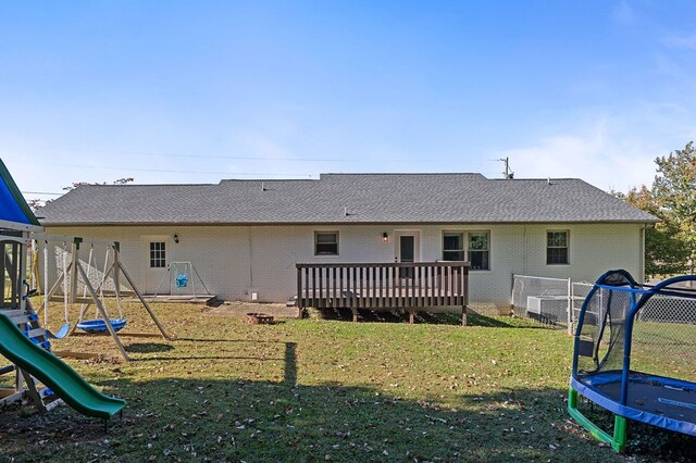 rear view of property with a deck, a yard, a trampoline, and a playground