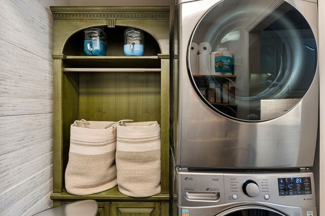 laundry room with laundry area, wooden walls, and stacked washer / dryer