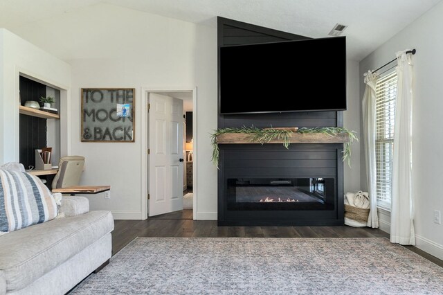 unfurnished living room with built in shelves, dark wood finished floors, a glass covered fireplace, vaulted ceiling, and baseboards