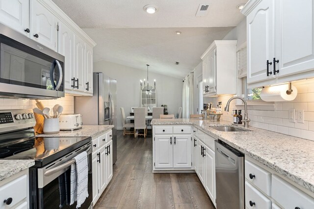 kitchen with lofted ceiling, hanging light fixtures, appliances with stainless steel finishes, white cabinets, and a sink