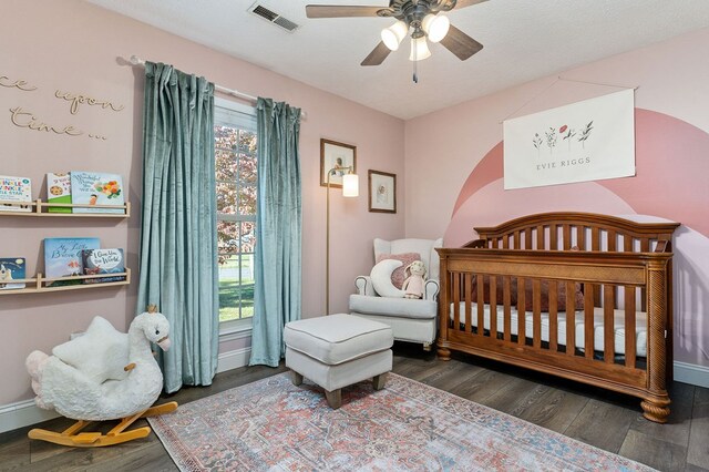 bedroom with baseboards, visible vents, dark wood finished floors, ceiling fan, and a nursery area