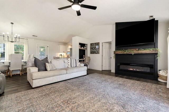 living area featuring lofted ceiling, ceiling fan with notable chandelier, dark wood-type flooring, and a glass covered fireplace