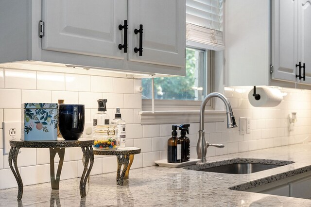 kitchen with a sink, decorative backsplash, and light stone countertops