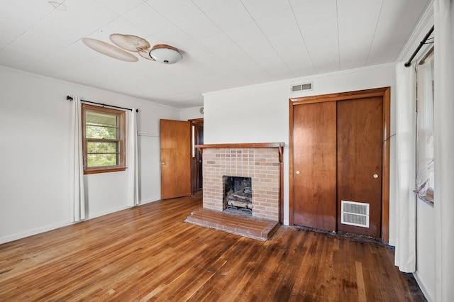 unfurnished living room featuring ornamental molding, a brick fireplace, visible vents, and wood finished floors