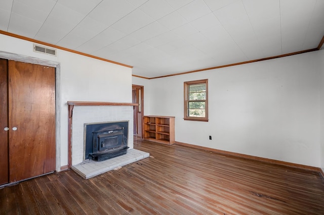 unfurnished living room with a wood stove, wood finished floors, visible vents, and crown molding