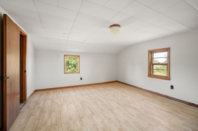 unfurnished room featuring a healthy amount of sunlight, light wood-style floors, baseboards, and vaulted ceiling