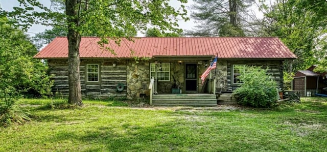 rear view of property with metal roof, stone siding, and a lawn