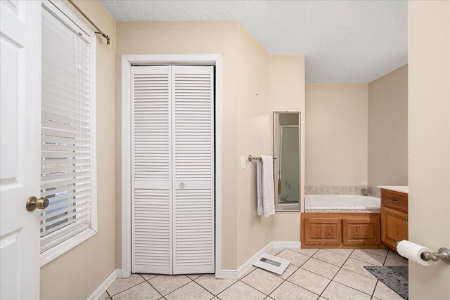 bathroom featuring a garden tub, a textured ceiling, a closet, and tile patterned floors