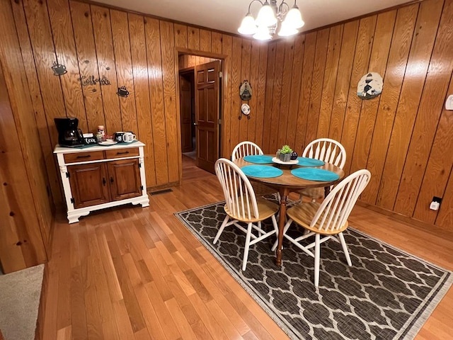 dining space with light wood-style floors, a chandelier, visible vents, and wood walls