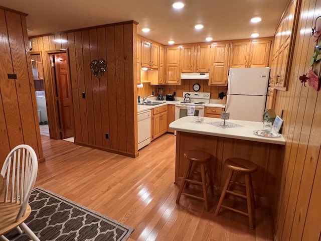 kitchen with light wood-style flooring, under cabinet range hood, white appliances, a kitchen breakfast bar, and light countertops