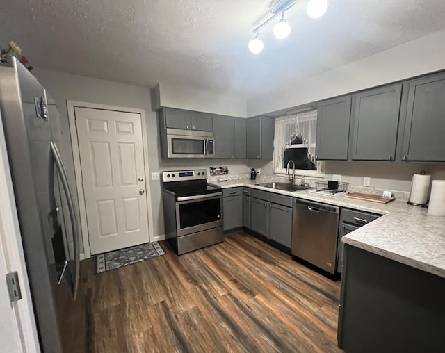 kitchen with stainless steel appliances, gray cabinets, dark wood-type flooring, a sink, and a textured ceiling