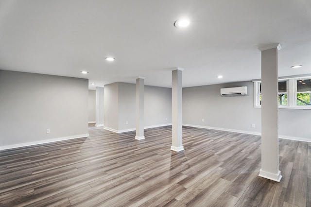 below grade area with recessed lighting, a wall mounted air conditioner, baseboards, and wood finished floors