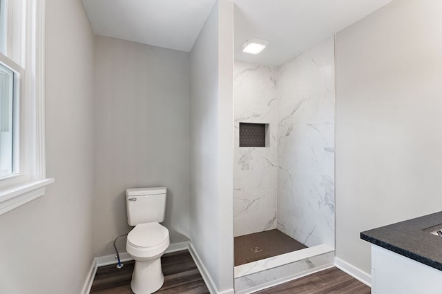 bathroom with a marble finish shower, toilet, vanity, wood finished floors, and baseboards