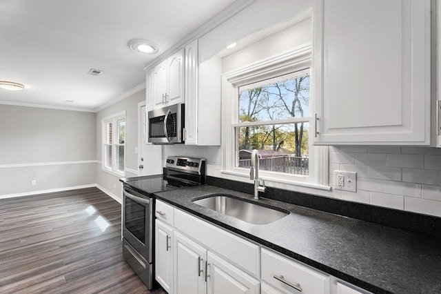 kitchen featuring stainless steel appliances, dark countertops, a sink, and white cabinetry