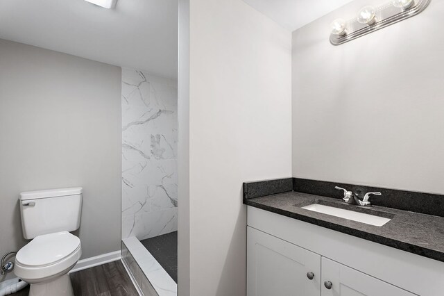 bathroom with toilet, a shower stall, vanity, wood finished floors, and baseboards