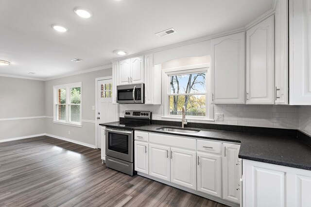 kitchen with dark wood finished floors, dark countertops, appliances with stainless steel finishes, white cabinetry, and a sink