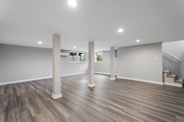 below grade area featuring dark wood-style flooring, recessed lighting, an AC wall unit, baseboards, and stairs