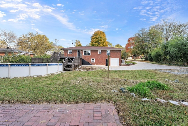 rear view of house featuring driveway, an attached garage, stairs, a deck, and a yard