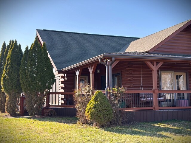 view of front of home featuring log siding, a porch, a front yard, and a shingled roof