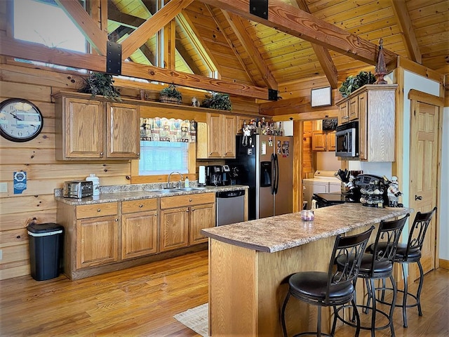 kitchen featuring washing machine and dryer, wood walls, light wood-style floors, stainless steel appliances, and a sink