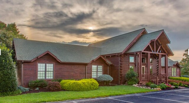 view of front of home with a lawn, uncovered parking, and a shingled roof