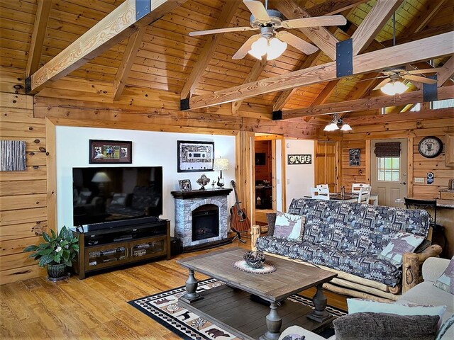 living area featuring wooden walls, ceiling fan, wood ceiling, a stone fireplace, and wood finished floors