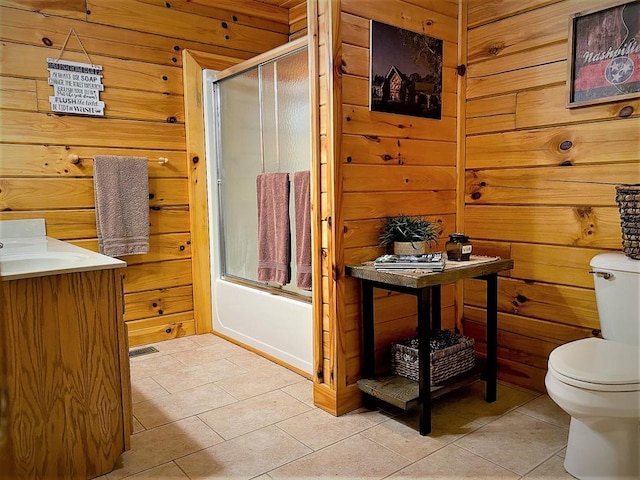 full bathroom with tile patterned flooring, wooden walls, toilet, and enclosed tub / shower combo