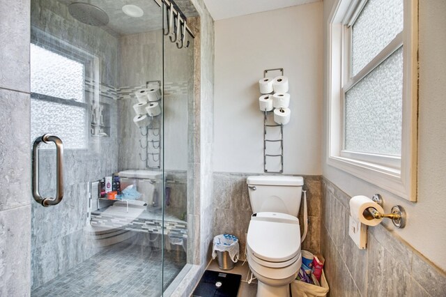 full bath with tile walls, wainscoting, a shower stall, and toilet